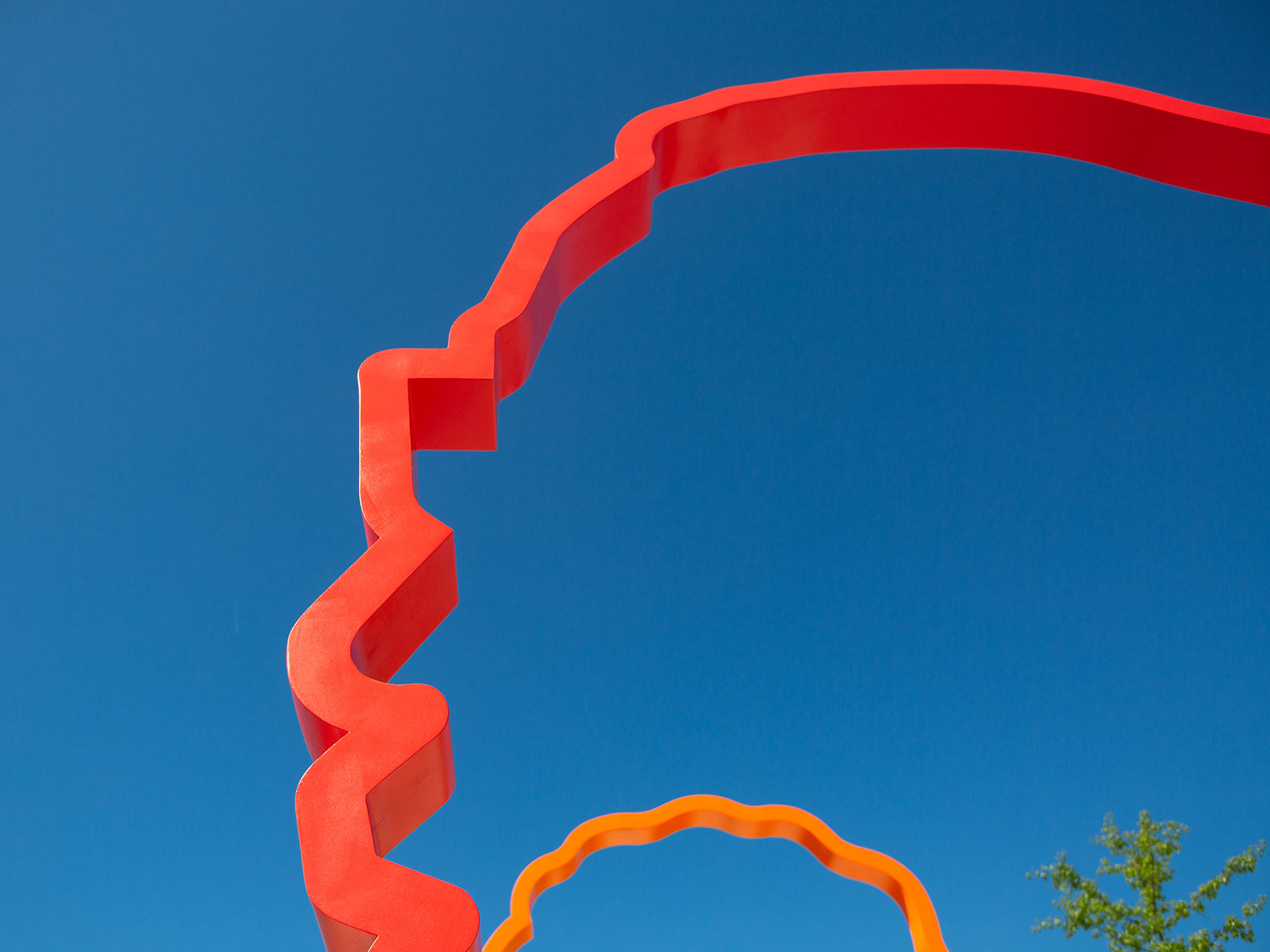 Detail of Harmonic Time, red an orange portraits against a blue sky. This public art installation is a new contemporary monument composed of a colonnade of three colorful monumental 12-foot-tall silhouette portraits in a gradient of orange, red, and purple.