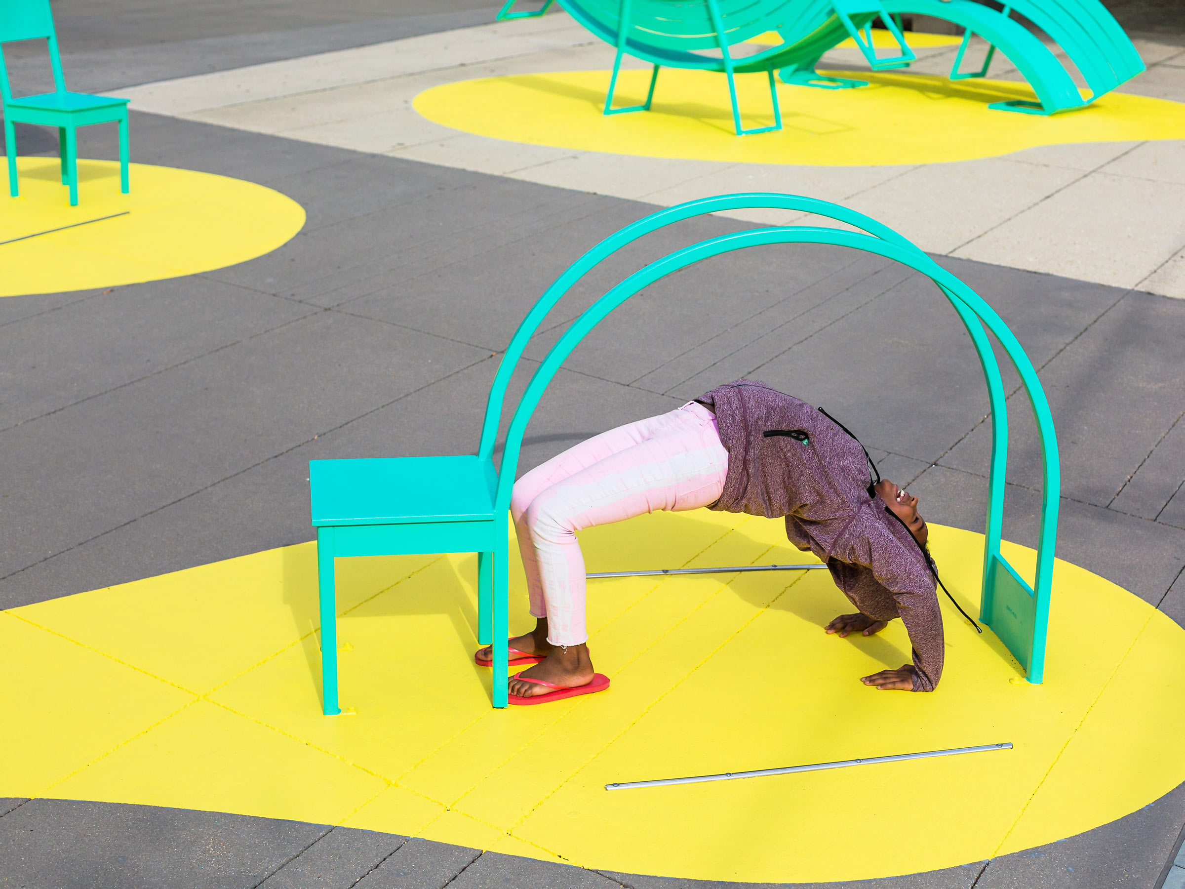 A girl does a backbend underneath a sculptural chair public art installation