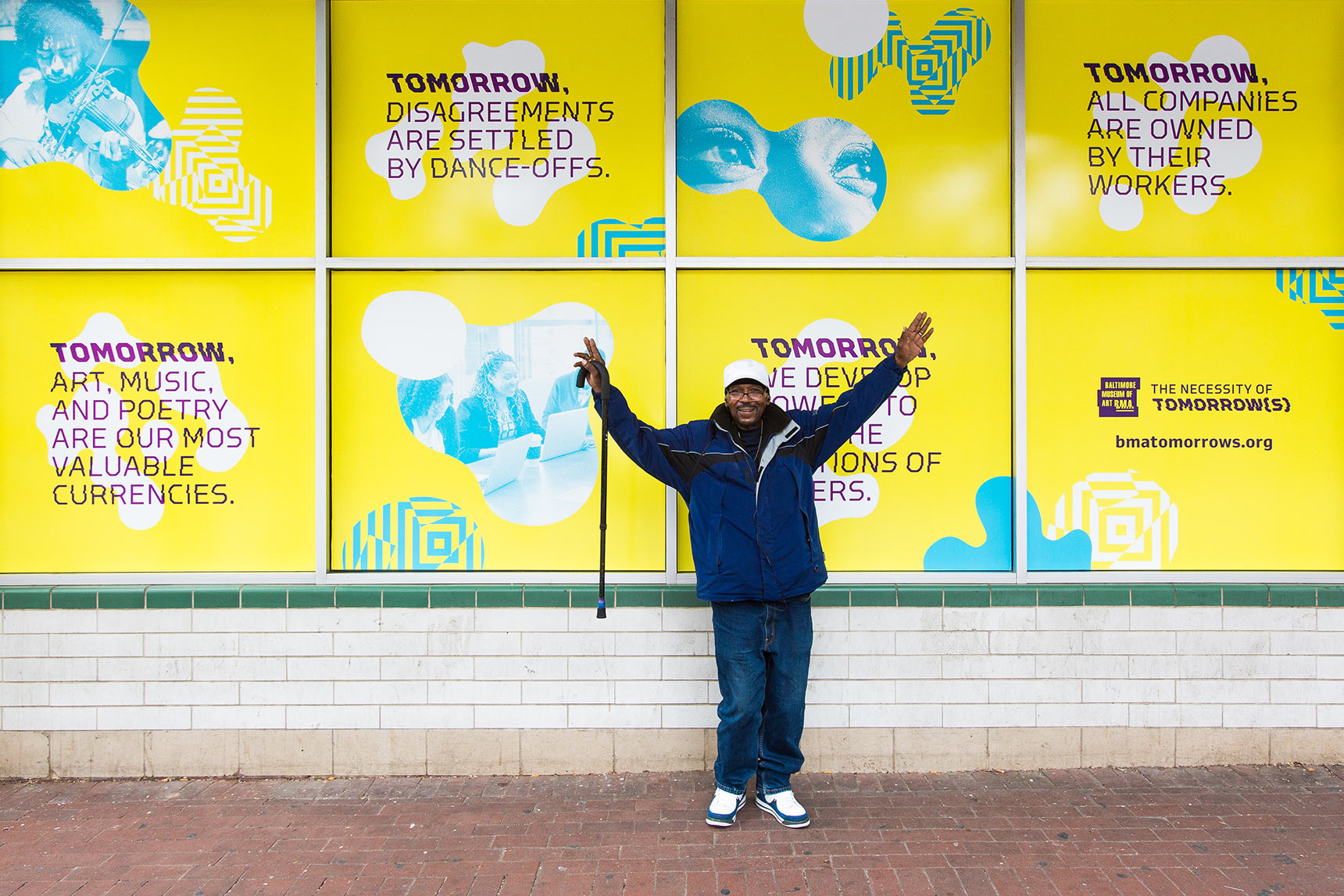 A man stands in front of an array of windows advertising Baltimore Museum of Art's Necessity of Tomorrow Lecture series