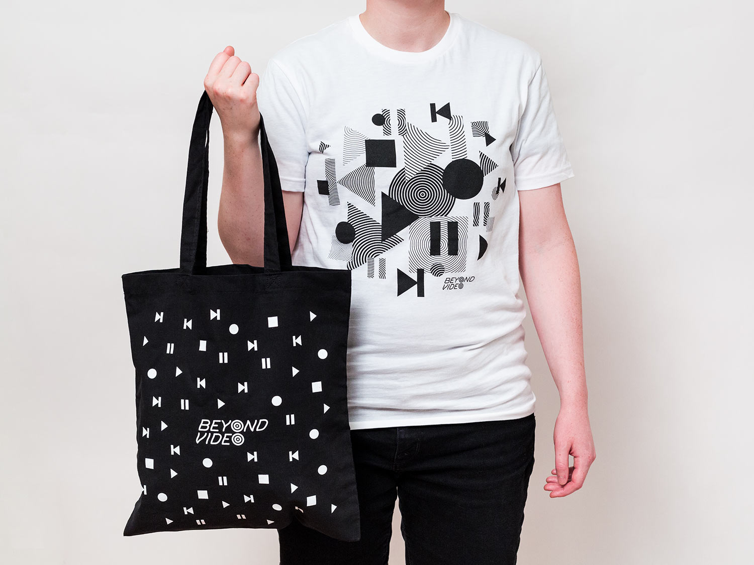 Black and white tote bag and T-shirt designs for Beyond Video, featuring a pattern of video and VHS control icons, part of brand identity for contemporary video store and lending library