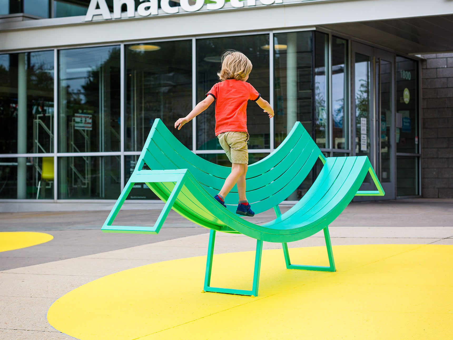 A boy plays on a curved sculptural bench, part of The Chairs, a sculptural seating public art installation in Washington DC.