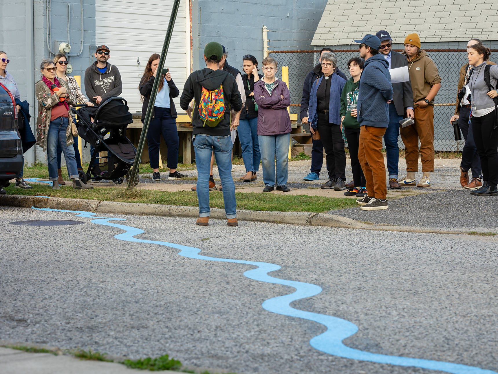A group of visitors attending a guided walking tour with Blue Water Baltimore and Bruce Willen as part of the Ghost Rivers public art project that follows the path of a buried creek in Baltimore.