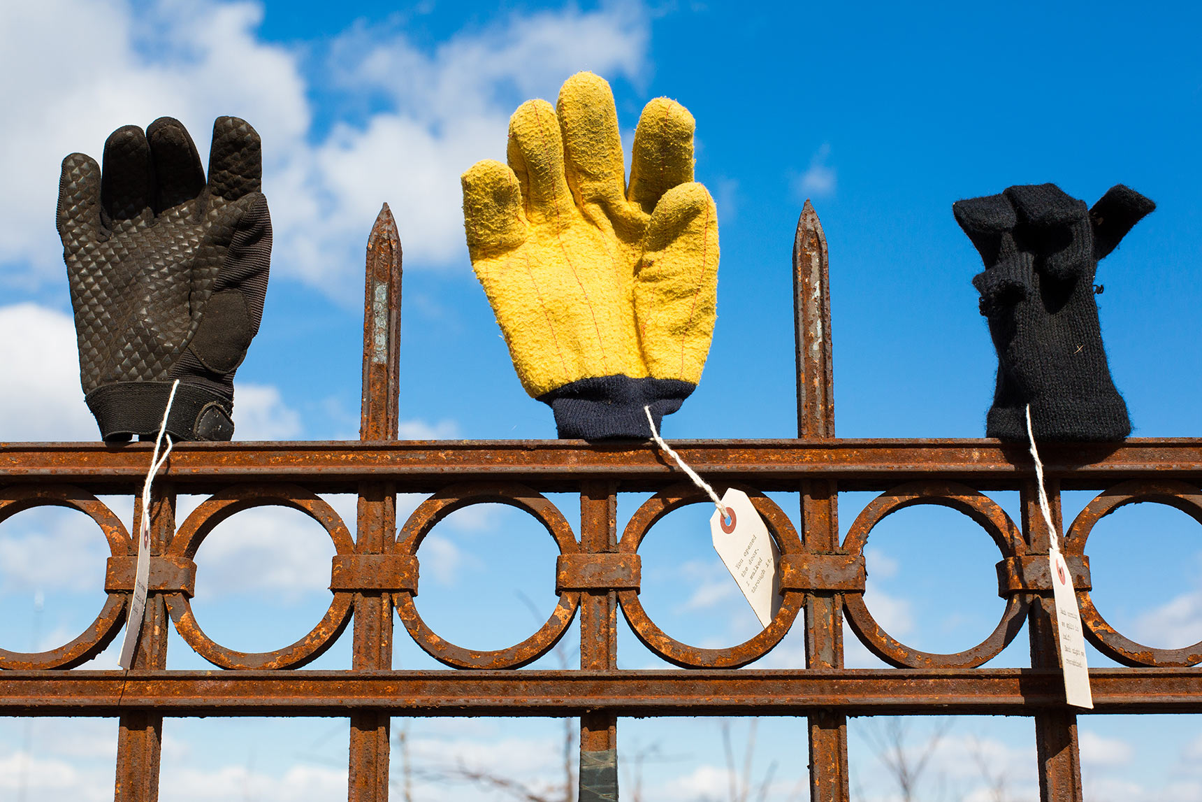 found gloves with notes displayed on a wrought iron fence in the Library of Lost Gloves & Lost Loves participatory public art installation by artist Bruce Willen