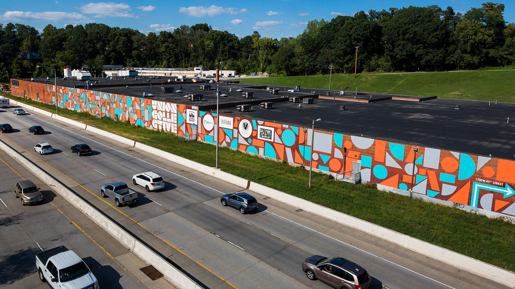 Massive mural on the side of the Union Collective warehouse building in baltimore composed of colorful orange, blue, and grey geometric shapes including circles, triangles, parallelograms, squares, etc.
