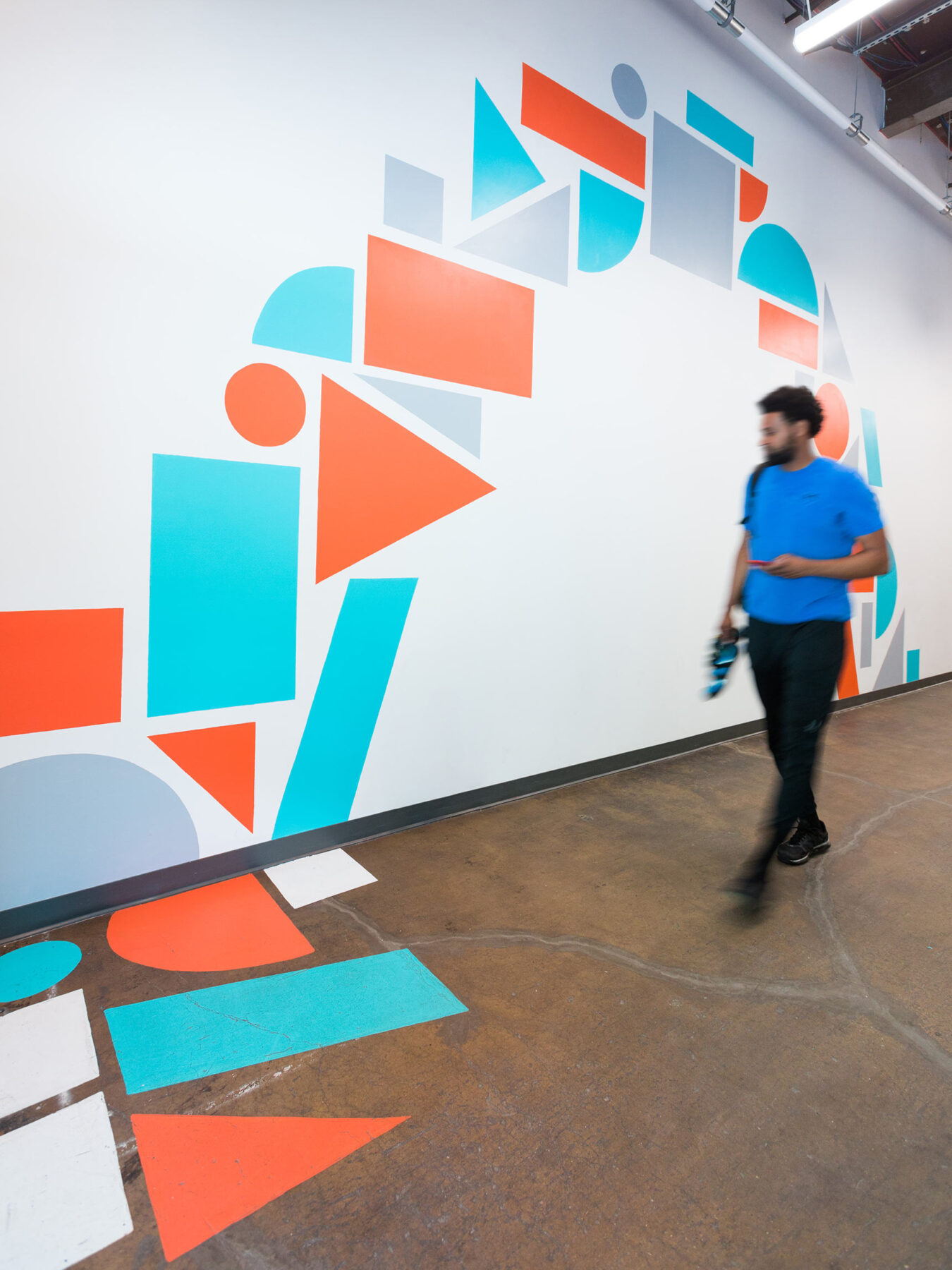 A man walking past colorful geometric shape supergraphic murals painted in the hallways and floors of the Union Collective building