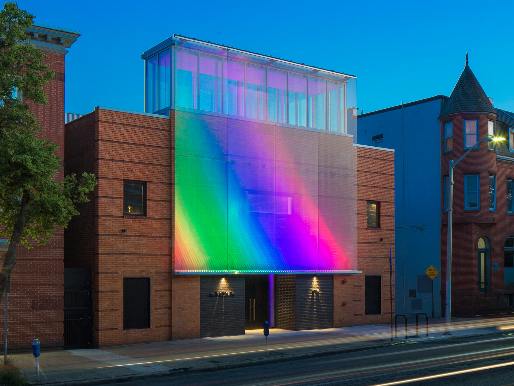 The exterior metal mesh screen facade of the Voxel Theater in Baltimore lit up at night in rainbow colors