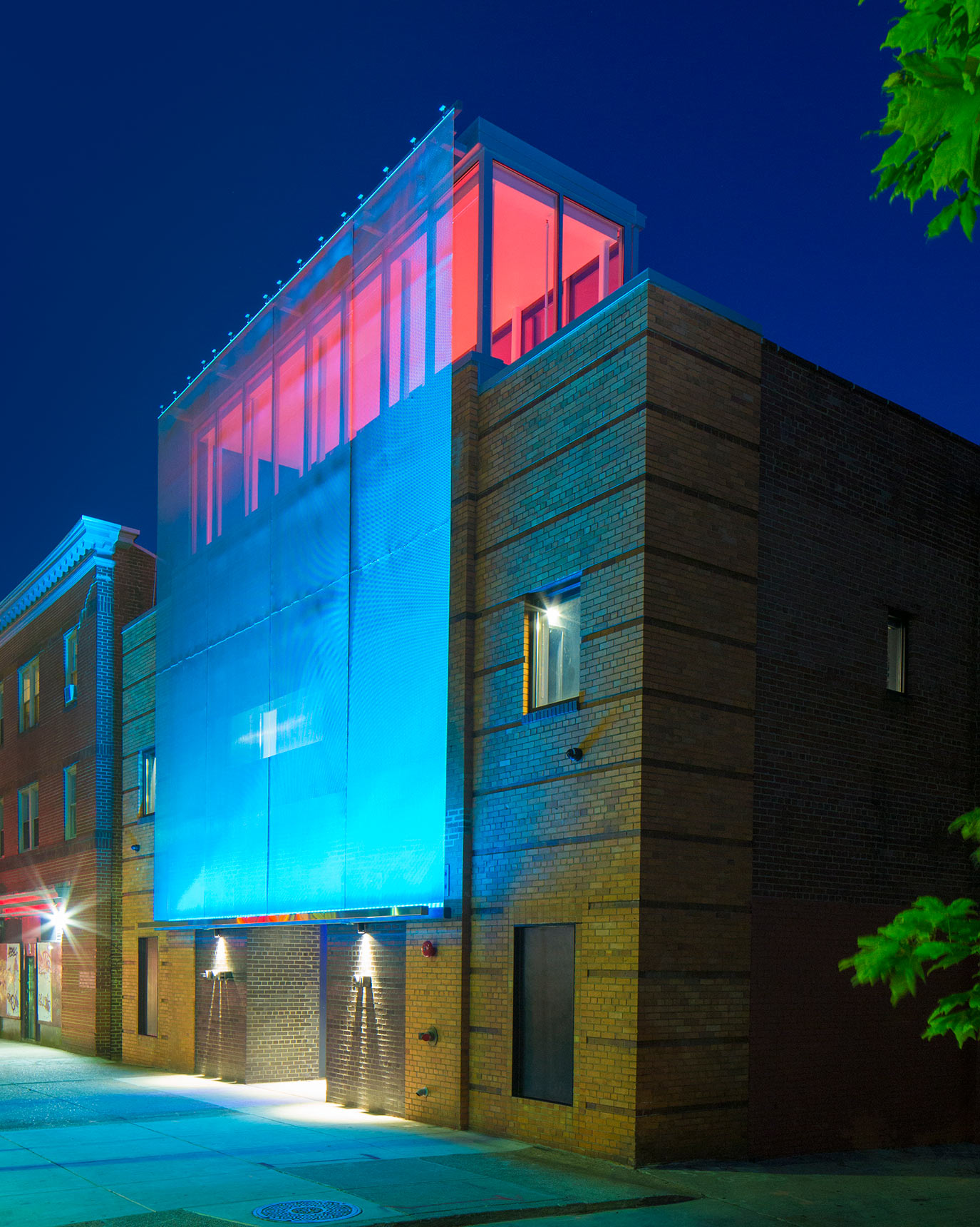 The exterior metal mesh screen facade of the Voxel Theater in Baltimore lit up at night in bright colors