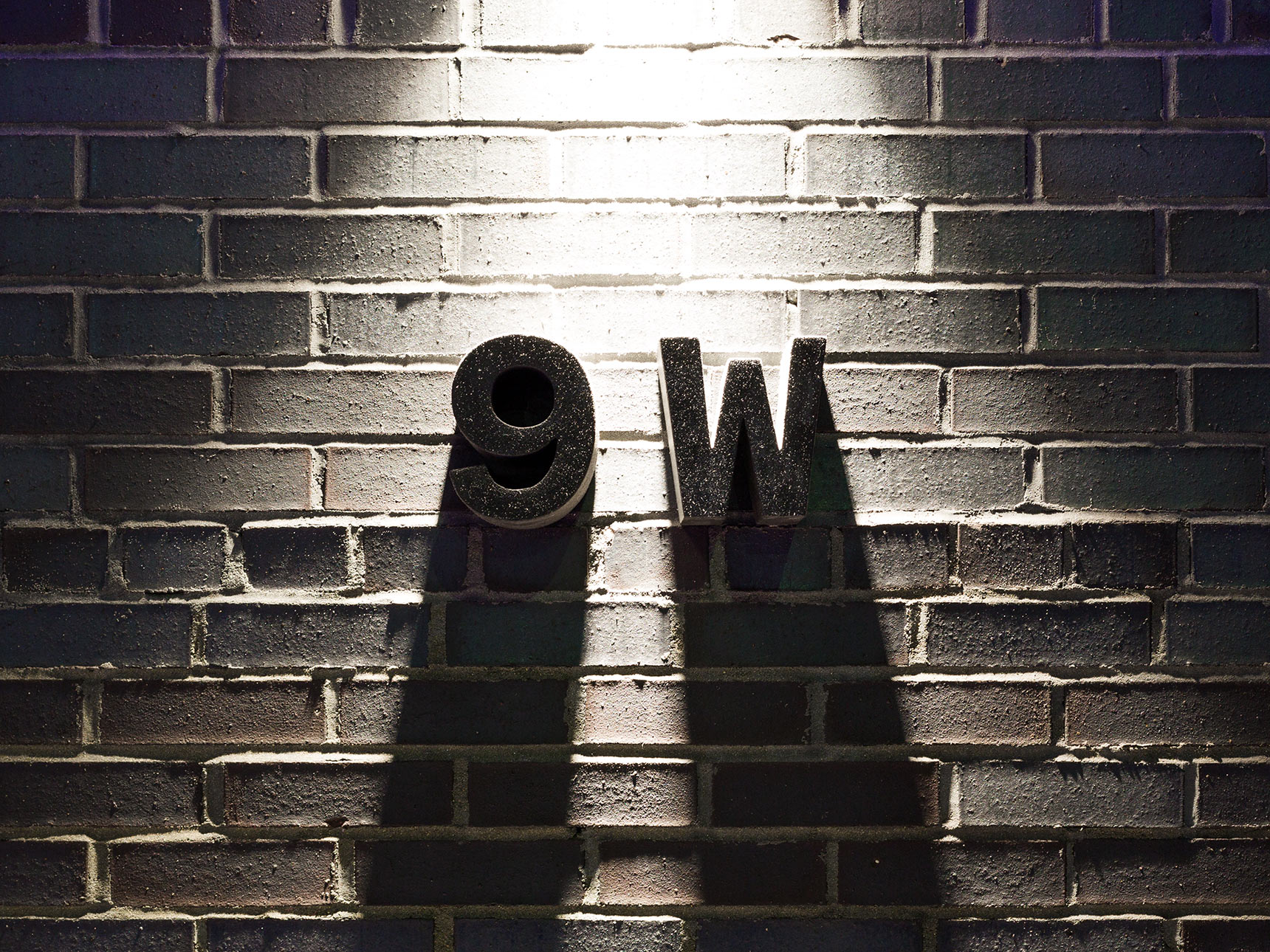 9W, black cast concrete dimensional signage on the the black brick facade of the Voxel Theater